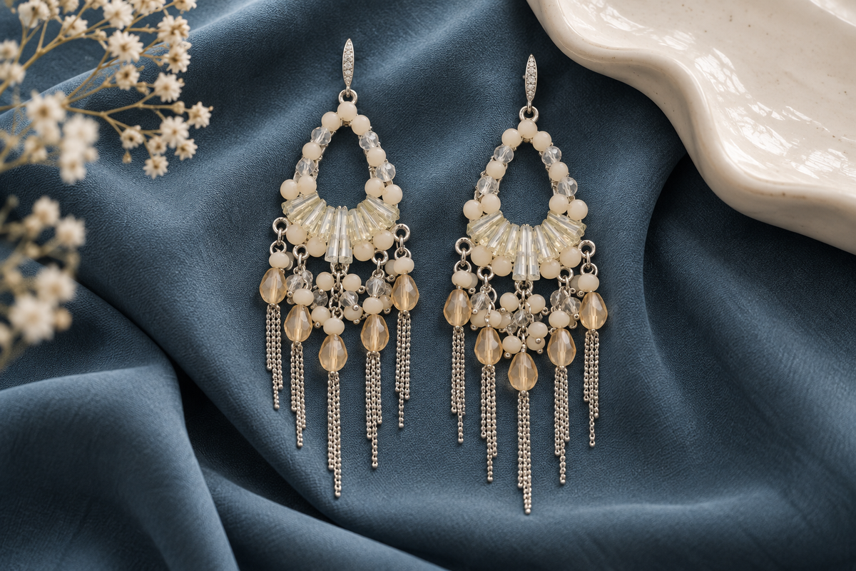 Pendientes Chandelier Perla Crema sobre un tejido azul, mostrando las cuentas claras, los colgantes y las cadenas plateadas.