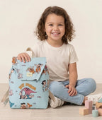 Niña llevando una mochila infantil azul claro con estampado de personajes prehistóricos