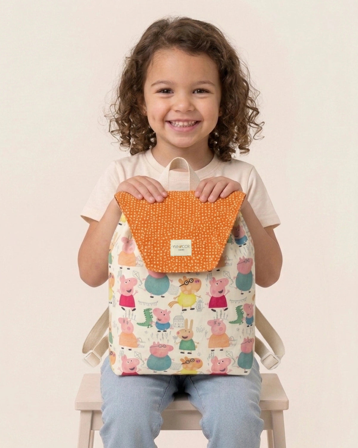 Niña llevando una mochila infantil con estampado de animalitos y solapa naranja